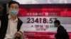 A man wearing a face mask walks past a bank's electronic board showing the Hong Kong share index at Hong Kong Stock Exchange Wednesday, March 25, 2020.