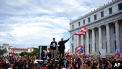 El rapero puertorriqueño René Juan Pérez, conocido como Residente, y Benito Antonio Martínez Ocasio, cuyo nombre artístico es Bad Bunny, animan a manifestantes frente al Capitolio antes de una marcha contra el gobernador Ricardo Rosselló, en San Juan, Puerto Rico.