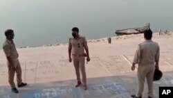 Esta imagen de un vídeo proporcionado por KK Productions muestra a oficiales de policía parados en la orilla de un río donde se encontraron varios cuerpos flotando, en el distrito de Ghazipur , Estado de Uttar Pradesh, la India, el 11 de mayo de 2021.