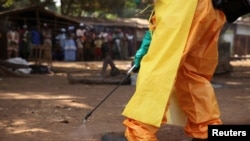 FILE - A member of the French Red Cross disinfects the area around a motionless person suspected of carrying the Ebola virus as a crowd gathers in Forecariah, Guinea, Jan. 30, 2015.