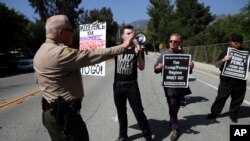 El sub jefe de la oficina del Sheriff del Conado de Los Ángeles pide a manifestantes que permanezcan en la acera frente al Laboratorio de Propulsión a Chorro de la NASA antes de la visita del vicepresidnete Mike Pence el sábado, 28 de abril, de 2018.