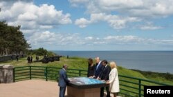 El presidente estadounidense Donald Trump, la primera dama estadounidense Melania Trump, el presidente francés Emmanuel Macron y su esposa Brigitte Macron reaccionan durante la conmemoración del día D en el cementerio y monumento estadounidense de Normandía en Colleville-sur-Mer, Francia. Junio 6,2019. Photo: VOA