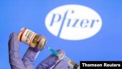 Una mujer sostiene una pequeña botella con una etiqueta que dice "Vacuna contra el coronavirus COVID-19" y una jeringuilla frente al logotipo de Pfizer. [Foto: Archivo]
