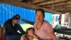 ស៊ឹម ស្រីអូន ដែលជាកម្មករកាត់ដេរត្រូវបានព្យួរការងារ កាលពីចុងខែមីនា កំពុងអង្គុយមើលកូនស្រី នៅក្រោមផ្ទះ ក្នុងភូមិពង្រ ឃុំស្វាយចចិប ស្រុកបរសេដ្ឋ ខេត្តកំពង់ស្ពឺ។ (ស៊ុន ណារិន/VOA)