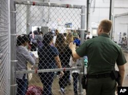 En esta foto provista por el Servicio de Aduanas e Inmigración, personal de la Patrulla Fronteriza vigila a personas que ha sido detenidas por ingresar ilegalmente a EE.UU. en McAllen, Texas, el domingo, 17 de junio de 2018.
