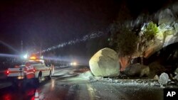 Equipos del Departamento de Transporte de California revisan grandes rocas que cayeron sobre la autopista 50, al este de Kyburz durante una tormenta en el Parque Nacional El Dorado, California, el domingo 1 de enero de 2023.