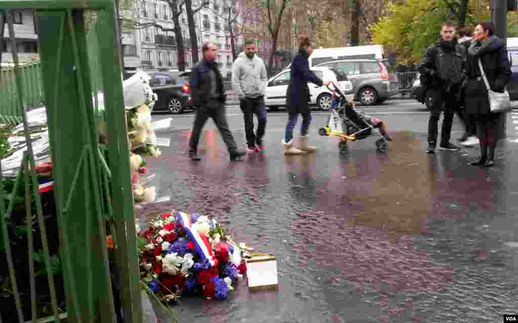 People walk past a plaque near Cafe Bonne Biere where jihadists shot dead 5 people last year, in Paris, Nov. 13, 2016. (L. Bryant/VOA)
