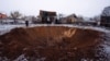 A local resident stands next to a crater at a site of a Russian missile strike, amid Russia's attack on Ukraine, in Kyiv, Ukraine Dec. 11, 2023. 