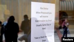 FILE - People who lost their jobs are reflected in the door of an Arkansas Workforce Center as they wait in line to file for unemployment following an outbreak of the coronavirus disease (COVID-19), in Fort Smith, Arkansas, April 6, 2020.