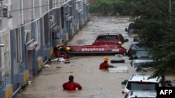 Petugas penyelamat mencari korban atau warga yang membutuhkan bantuan di dekat kendaraan di tempat parkir, bagian bawah bangunan apartemen yang tergenang banjir akibat hujan lebat di kota Daejeon, Korea Selatan (foto: dok). 
