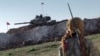 FILE - A Syrian Kurdish militia member of the YPG patrols near a Turkish army tank as Turks work to build a new Ottoman tomb in the background in Esme village in Aleppo province, Syria, Feb. 22, 2015.