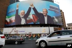 Spanduk besar yang memperlihatkan mendiang pemimpin Hamas Ismail Haniyeh, kiri, bergandengan tangan dengan Presiden Iran Masoud Pezeshkian, di sebuah alun-alun di pusat kota Teheran, Iran, Senin, 5 Agustus 2024. (Foto: AP)