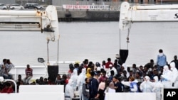 Activistas levantan una pancarta que dice "Detengan el ataque a los refugiados" mientras inmigrantes aguardan para desembarcar del barco "Diciotti" de la Guardia Costera italiana, en el puerto siciliano de Catania, en el sur de Italia, el miércoles 13 de junio de 2018.