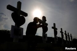Un hombre escribe un mensaje en una de las cruces colocada en honor de las víctimas del tiroteo en la escuela secundaria Santa Fe, en Santa Fe, Texas. Mayo 21, 2018.