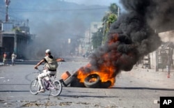 Un hombre pasa en bicicleta frente a neumáticos incendiados por manifestantes que exigen saber cómo se usaron los fondos de Petrocaribe. Puerto Príncipe, Haití, miércoles 17 de octubre de 2018.