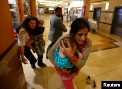 Women carrying children run for safety as armed police hunt for gunmen who went on a shooting spree in Westgate shopping center in Nairobi, Kenya, Sept. 21, 2013.