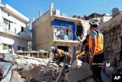 This June 26, 2018, photo, provided by Nabaa Media, a Syrian opposition media outlet, shows civil defense workers and civilians inspecting damaged buildings that were hit by Syrian government forces bombardments, in Daraa, southwestern Syria.