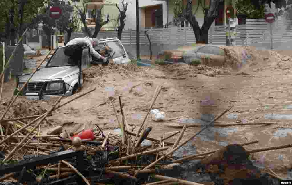 A woman is rescued from flood waters by a resident standing on top of her car during heavy rain in Chalandri suburb north of Athens, Greece, Feb. 22, 2013. 