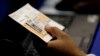 FILE - An election official checks a voter's photo identification at an early voting polling site in Austin, Texas.