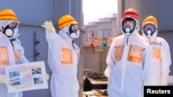 Japan's Prime Minister Shinzo Abe (2nd R), wearing protective suit and mask, is briefed about tanks containing radioactive water by Fukushima Daiichi nuclear power plant chief Akira Ono (2nd L), as they stand near a tank (C, with railings painted red and 