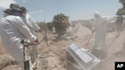 Unos trabajadores portan equipo de protección mientras realizan un entierro el martes 19 de mayo de 2020 en una zona del cementerio municipal de San Rafael, destinada para los casos de COVID-19 en Ciudad Juárez, México. 