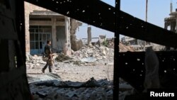 A Free Syrian Army fighter carries his weapon as he walks past damaged buildings in a rebel-held part of the southern city of Deraa, Syria, July 9, 2017.