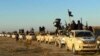 FILE - In this undated file photo released by a militant website, which has been verified and is consistent with other AP reporting, militants of the Islamic State group hold up their weapons and wave its flags on their vehicles in a convoy to Iraq, in Ra