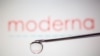Moderna logo is reflected in a drop on a syringe needle