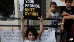 A girl holds a peace message during a peace protest at Ladras or Lokmachi crossing point that connects the Greek Cypriot south and the Turkish Cypriots breakaway north, inside the U.N buffer zone in central divided capital, Nicosia, Cyprus, July 6, 2017. 