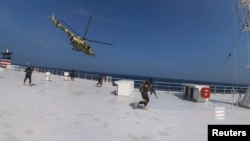 Houthi military helicopter hovers over the Galaxy Leader cargo ship as Houthi fighters walk on the ship's deck in the Red Sea