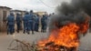 Burundian riot police march past a burning tyre roadblock following clashes with opposition protesters in a street in the capital Bujumbura, April 26, 2015.