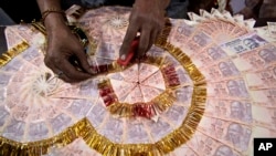 FILE - A shopkeeper prepares a garland with Indian 10 rupees denomination notes (USD $0.15) for sale, especially for wedding season, in Jammu, India, Friday, Nov. 11, 2016.
