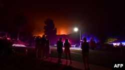 People watch as the Bobcat Fire burns on hillsides behind homes in Arcadia, California on September 13, 2020 prompting mandatory evacuations for residents of several communitu - California wildfires have shrouded much of the western United States in…