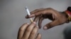 FILE - A man passes a cigarette to another as they sit on a pavement along a road in New Delhi, India, Aug. 18, 2015. 