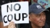 A Thai anti-coup protester holds a banner during a protest outside a shopping complex in Bangkok, Thailand Saturday, May 24, 2014. Thailand's coup leaders said Saturday that they would keep former Prime Minister Yingluck Shinawatra, Cabinet members and an