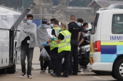 Border Force officers escort a group of men thought to be migrants to a waiting bus in the port city of Dover, England, Aug. 8, 2020.