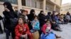 A picture taken on March 13, 2018 shows evacuated civilians and children sitting in the yard of a school lying on the government side of the Wafideen checkpoint on the outskirts of the Syrian capital Damascus neighboring the Eastern Ghouta enclave.