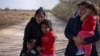 Dos solicitantes de asilo guatemaltecas con sus hijos esperan por transportación tras cruzar el Río Grande desde México a Texas, EE. UU., en una balsa el 10 de marzo de 2021.