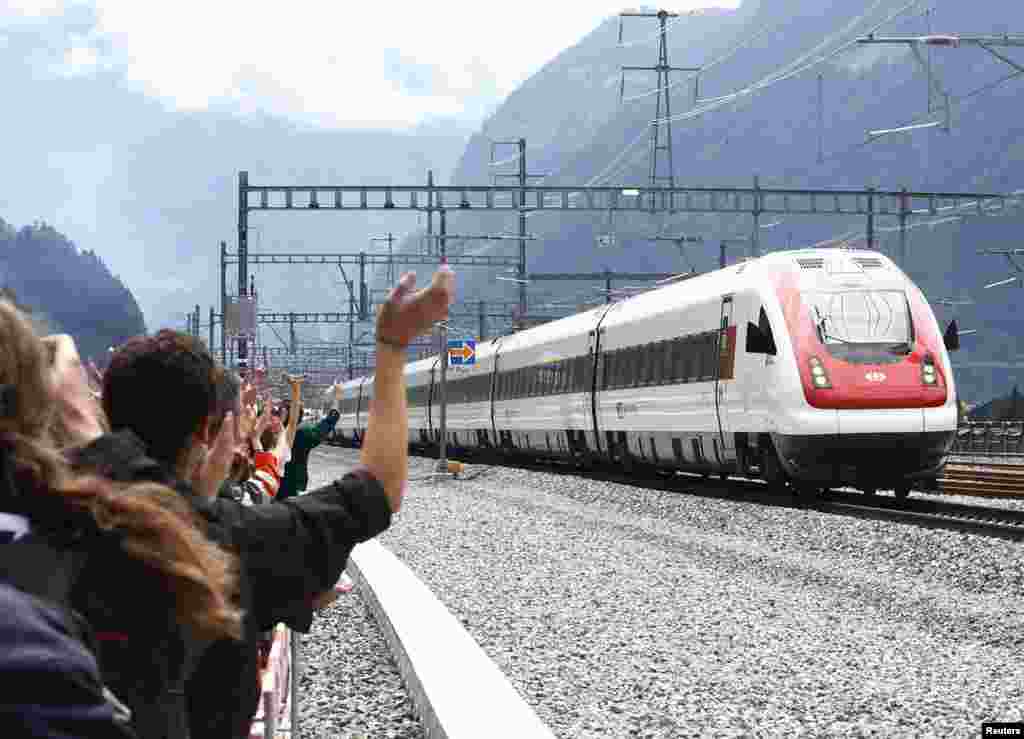 Para tamu melambai ke arah kereta api yang baru saja melalui terowongan kereta terpanjang di dunia &#39;NEAT Gotthard&#39; sepanjang 57,1-km di bawah pegunungan Alpen di Swiss.