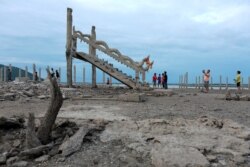 People walk and take pictures at the ruins of a Buddhist temple which has resurfaced in a dried-up dam due to drought, in Lopburi, Thailand, Aug. 1, 2019.