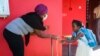 FILE - A staff member, wearing a protective facemask, helps a student to wash her hands at Malamani Primary School, in Chirongui, on the French Indian Ocean island of Mayotte, May 27, 2020.