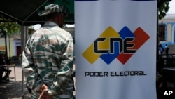 Un miembro de la milicia se detiene al lado de un banner del Consejo Nacional Electoral (CNE) en un punto de inscripción en el Registro Electoral. Archivo (AP Photo/Ariana Cubillos)
