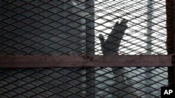 FILE - A defendant, caged in a courtroom, raises his hand, in Torah prison, southern Cairo, Egypt, Aug. 22, 2015. The U.N. has condemned the recent execution in Egypt of 20 men on alleged terrorist-related charges.