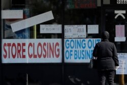 FILE - A woman looks at signs at a store closed due to the coronavirus pandemic, in Niles, Illinois, May 13, 2020.