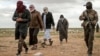 Men suspected of being an Islamic State (IS) group's fighter walk next to a member of the Kurdish-led Syrian Democratic Forces (SDF) as they wait to be searched after leaving the IS group's last holdout of Baghouz, Syria, Feb. 27, 2019.