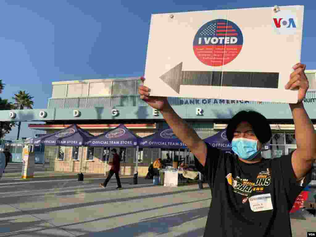 Un joven en el Dodger Stadium, usado como centro de votación cerca de Elysian Park en Los Ángeles, sostiene un cartel previo al cierre del centro. noviembre 3 de 2020.