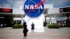 FILE - Tourists take pictures of a NASA sign at the Kennedy Space Center visitors complex in Cape Canaveral, Florida.