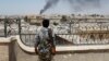 FILE - A Kurdish fighter from the People's Protection Units looks at the damage after an coalition airstrike in Raqqa, Syria, June 16, 2017. 
