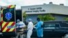 Un enfermo de coronavirus en Miami llega en ambulancia a un hospital especializado, mientras otro es sacado en un carro fúnebre.