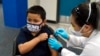 Eric Aviles, de 6 años, recibe la vacuna Pfizer COVID-19 de la farmacéutica Sylvia Uong en una clínica de vacunación pediátrica para niños de 5 a 11 años establecida en la Escuela Intermedia Willard en Santa Ana, California, el 9 de noviembre de 2021.